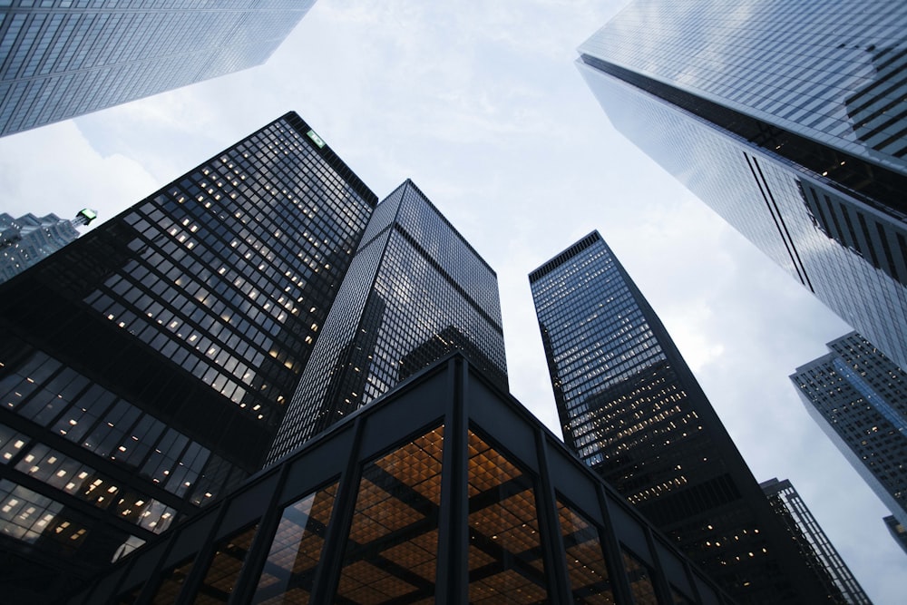 Looking up at dark corporate skyscrapers against a moody sky, luxury business aesthetic, dark gold tint, no people